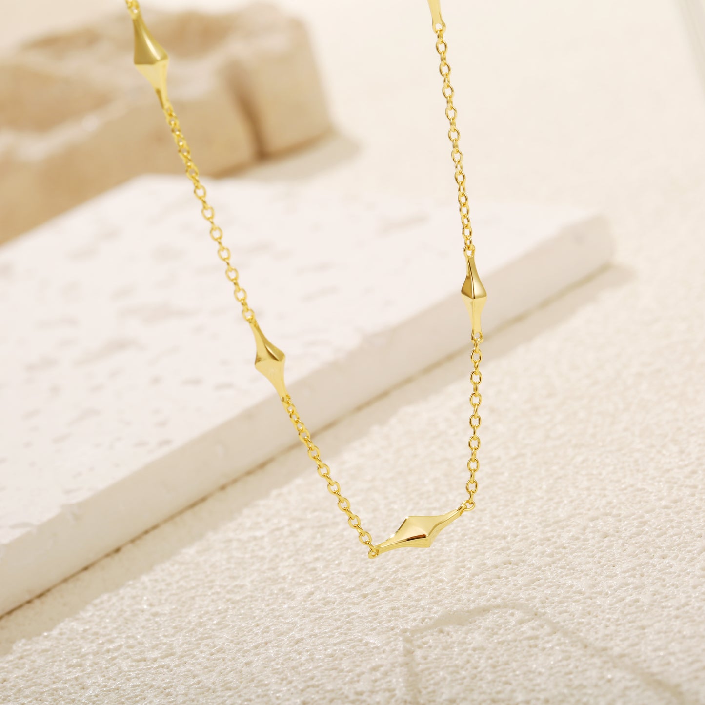 Elegant gold vermeil necklace with geometric kite-shaped charms evenly spaced along a delicate chain